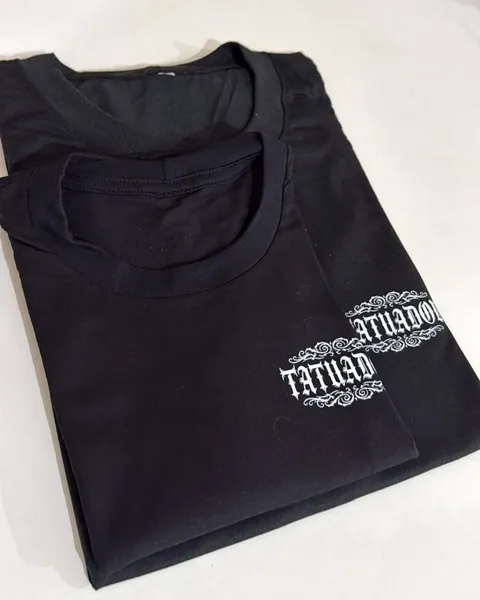 Duas camisetas pretas dobradas com o logo Tatuador em branco no peito